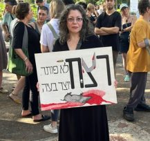אישה לבושה בשימלה שחורה, מחזיקה שלט בהפגנה נגד ירי בחזירי בר בחיפה.