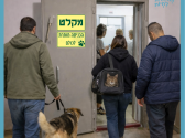 חדר מדרגות ובו דלת מקלט פתוחה ועליה שלט: "הכניסה מותרת לכולם". אדם עם כלב מוחזק ברצועה, אישה עם תיק ובו חתול ואדם במעיל כחול, נכנסים למקלט.